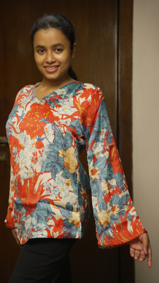 Woman wearing a colorful floral blouse standing in front of a wooden door.