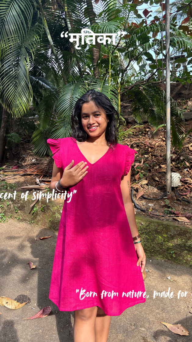 Woman in a pink dress standing outdoors with greenery in the background