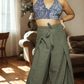 Woman wearing a blue patterned top and green wide-leg pants in a living room.