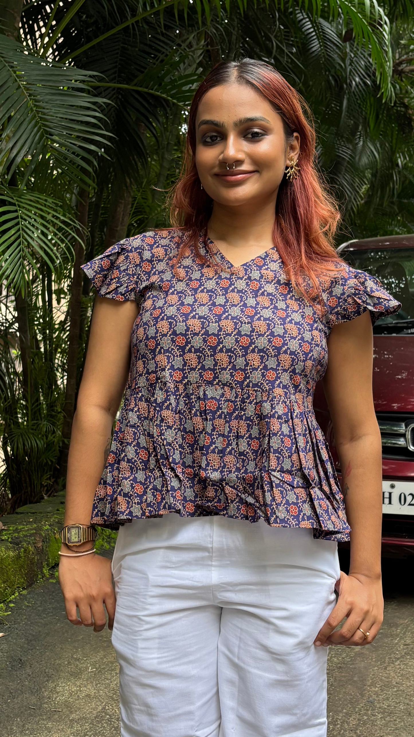 Woman standing outdoors with greenery and a car in the background