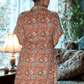 Woman wearing a patterned dress standing in a room with curtains and a lamp.