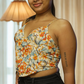 Woman wearing a floral top and black pants in a room with curtains and a lamp.