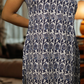 Woman wearing a sleeveless blue and white patterned dress in a room with a lamp and sofa.