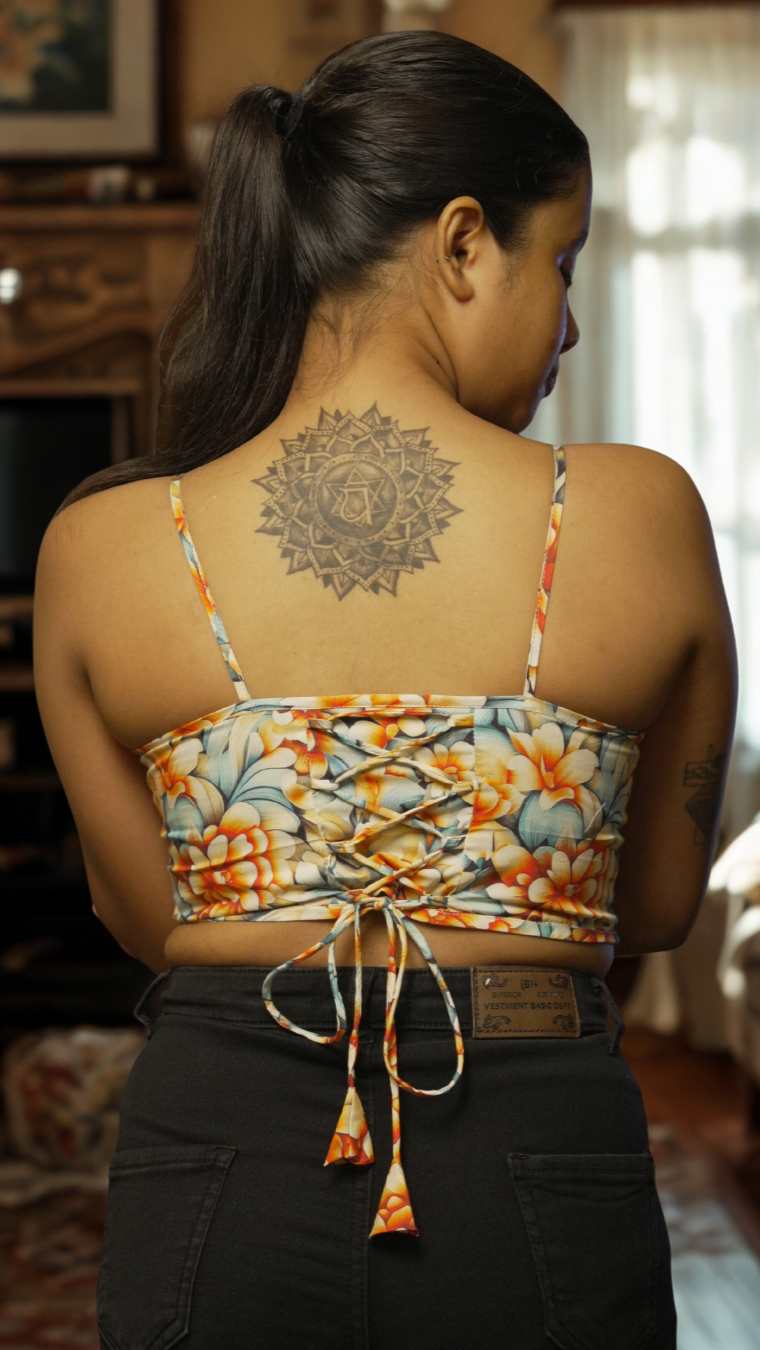 Woman wearing a floral top with a tattoo on her back in a living room setting