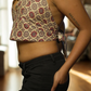Woman wearing a patterned top and black pants in a room with wooden floor and furniture.