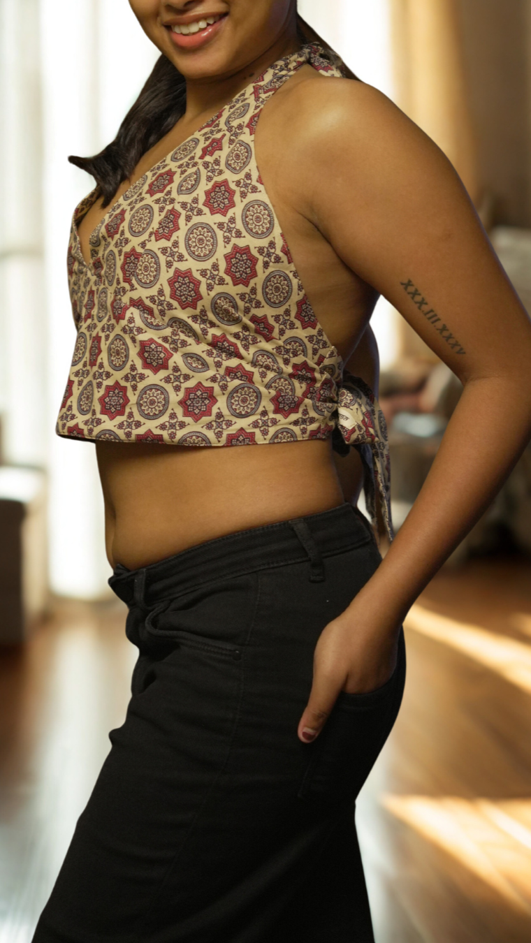 Woman wearing a patterned top and black pants in a room with wooden floor and furniture.