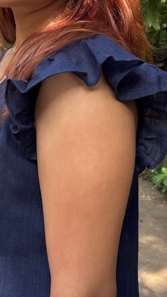 Person wearing a blue dress with ruffled sleeves in an outdoor setting