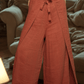 Person wearing a blue patterned top and rust-colored wide-leg pants indoors.