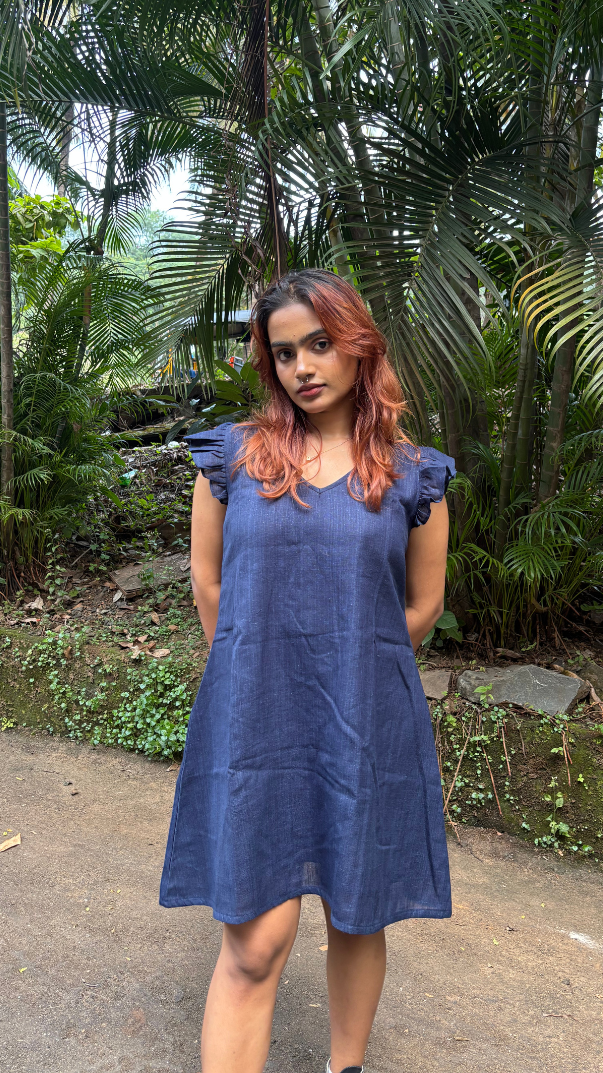 Woman in a blue dress standing in a tropical setting with palm trees.