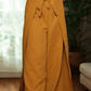 Person wearing a blue patterned crop top and mustard yellow wide-leg pants indoors.