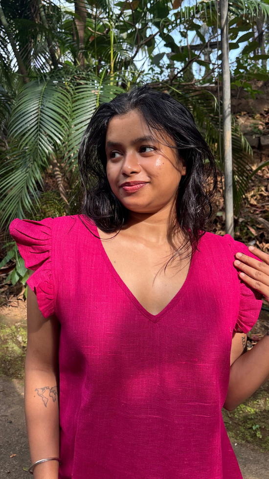 Woman in a pink dress standing outdoors with greenery in the background