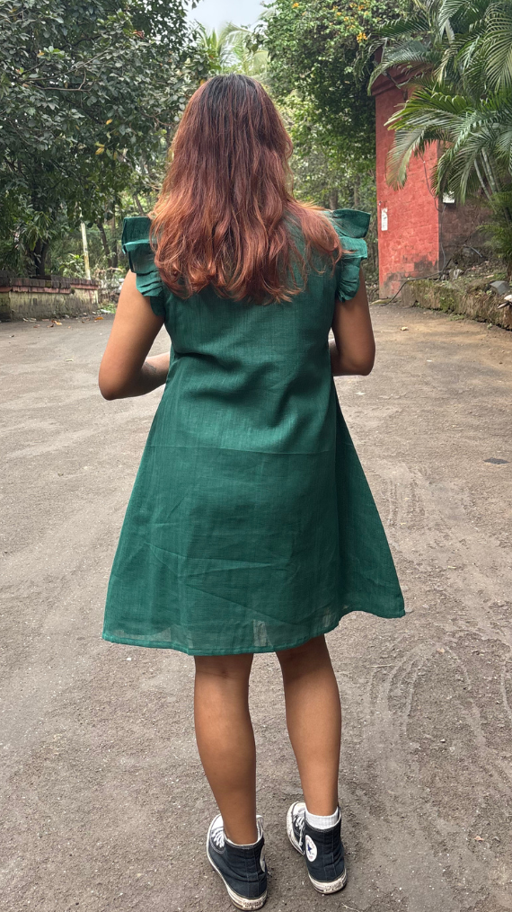 Person wearing a green dress standing on a road with trees and a red building in the background
