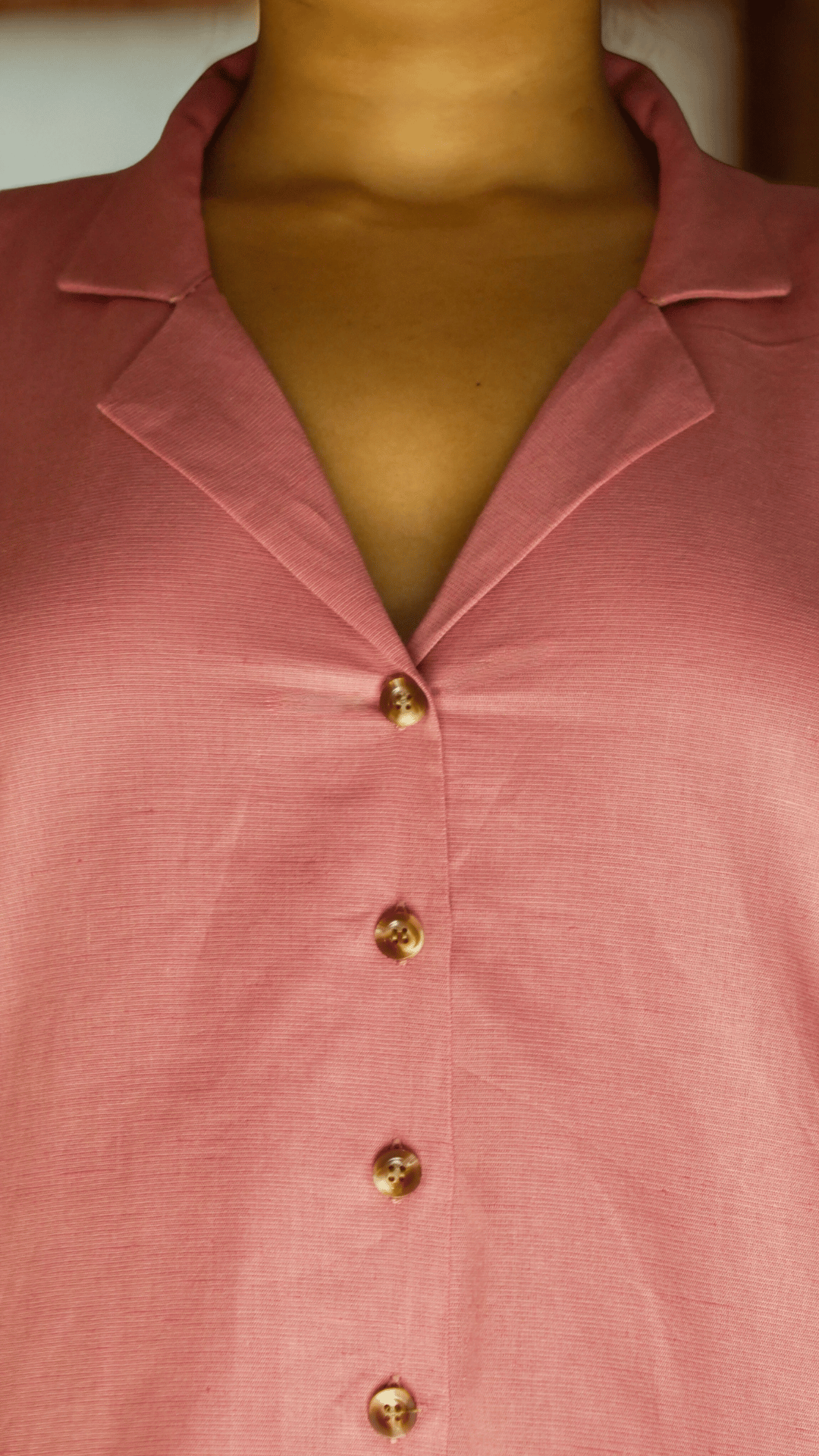 Close-up of a pink shirt with gold buttons on a plain background